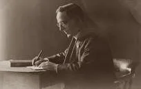 A vintage portrait of a man in a black suit writing at a desk.